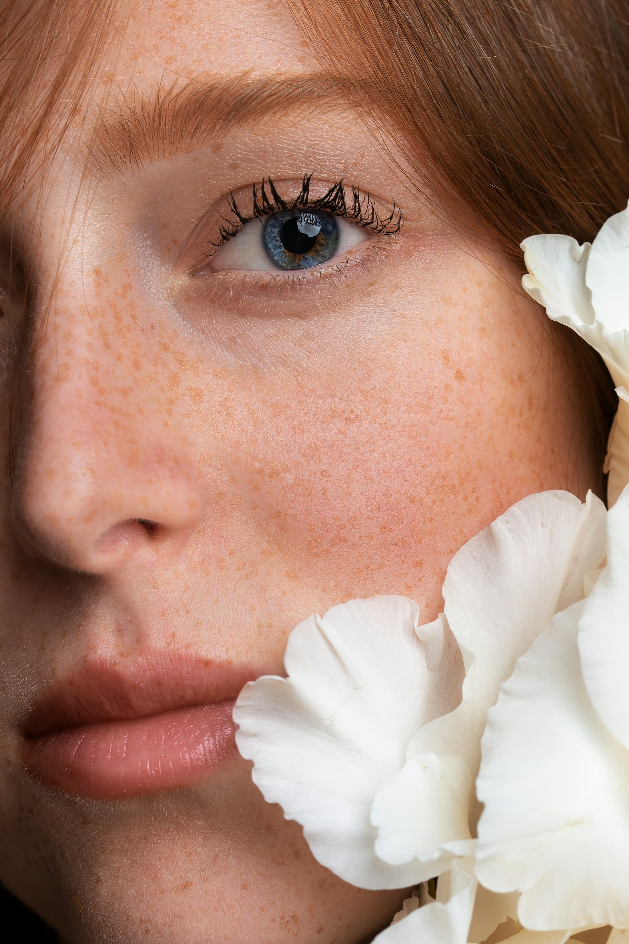 Editorial close-up of a model with healthy, glowing skin, white petals beside her face